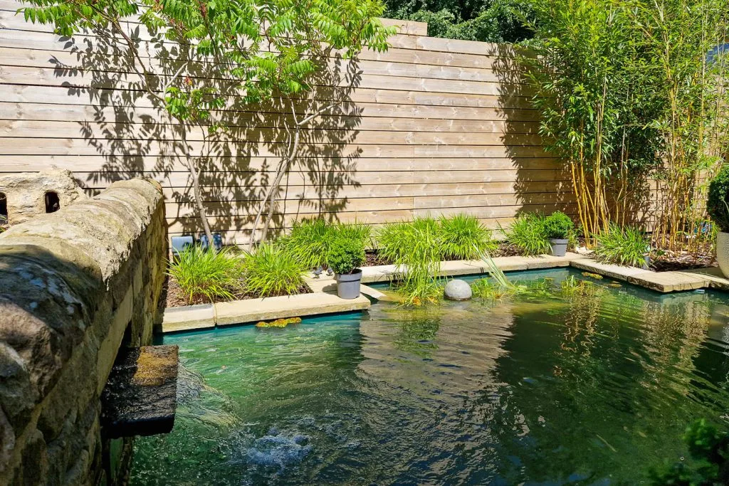 An impressive Victorian semi backing onto the woods demanded a garden to complement it.
Given the character of the property we used Yorkstone throughout for both paving and walls.
The garden is split by a drystone which houses a large stone water blade, discharging into an equally large pond. There is a large dining patio covered by a chunky oak pergola and a large Acer is surrounded by a perennial meadow. The upper garden is mainly lawn and planting with a smaller watercourse and then irregularly shaped steps leading up to the house. Outside the backdoor is a made to measure log and bin store.